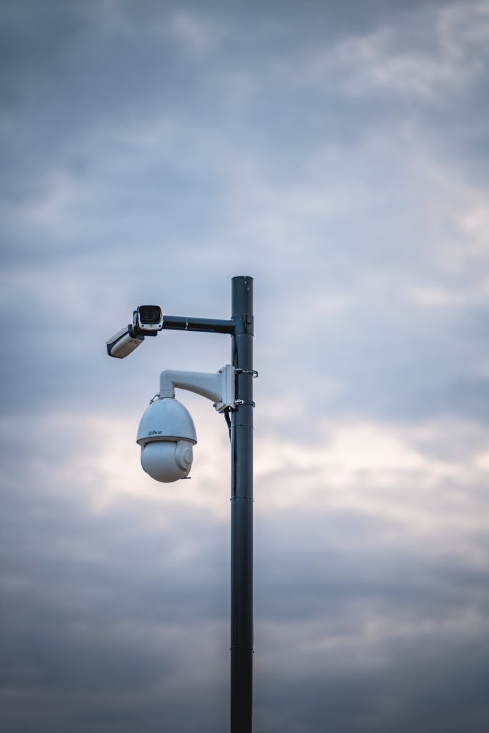 Security cameras mounted on a pole under a cloudy sky emphasize surveillance and protection.