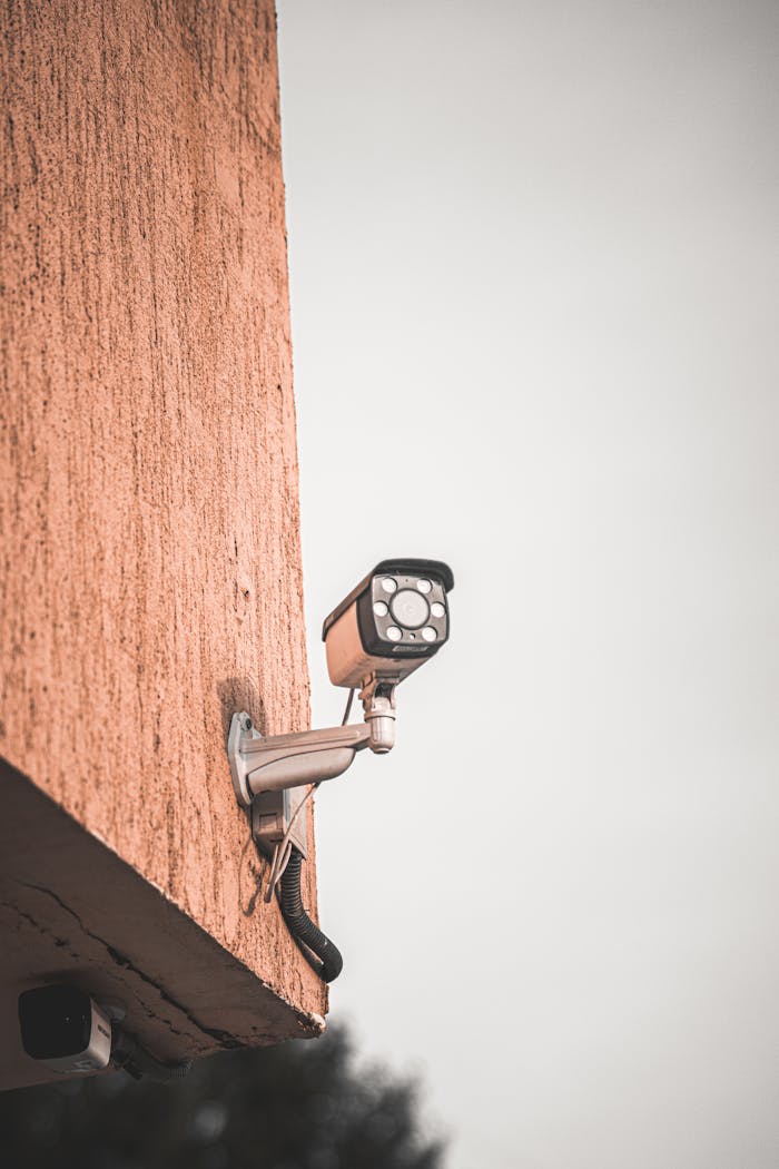 gallery-6 Close-up of a security camera mounted on a building wall, capturing urban safety measures.