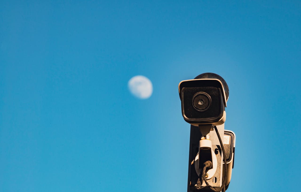 A CCTV surveillance camera with a blue sky and moon in the background, capturing urban security essence.